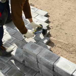 Hands of a worker installing concrete blocks, paving slabs with a rubber hammer